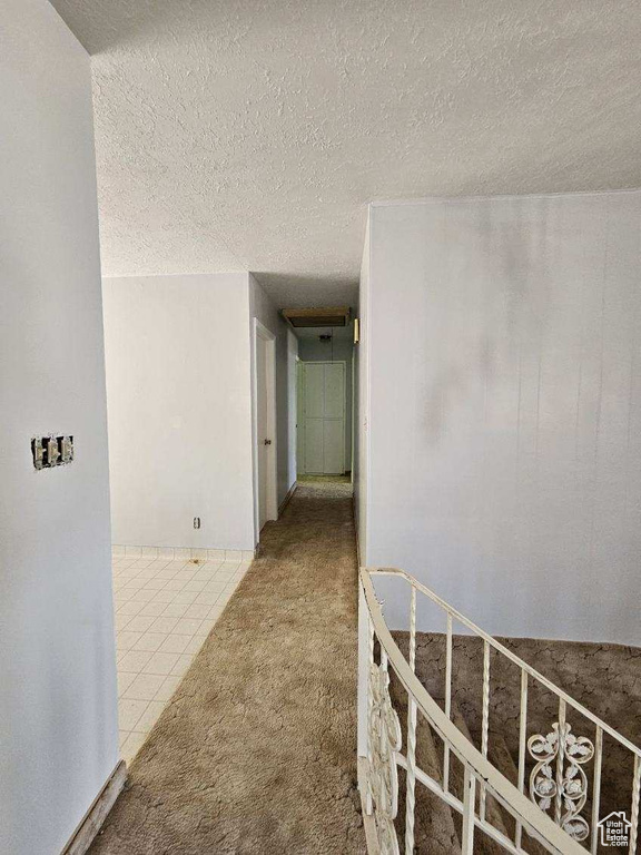 Hallway featuring carpet, a textured ceiling, and tile patterned flooring