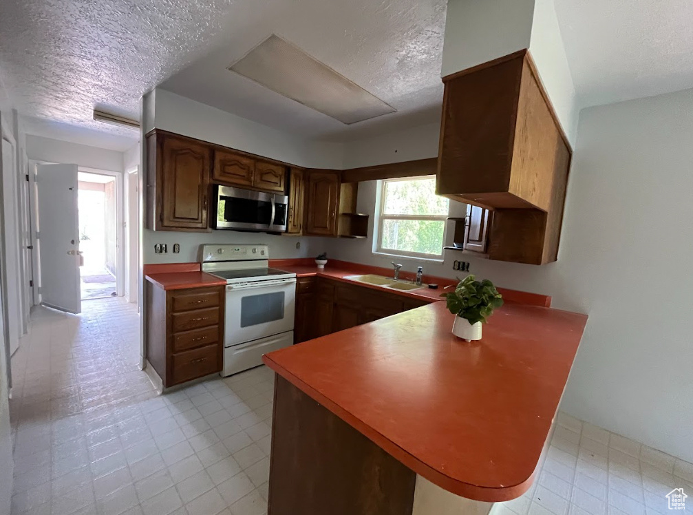 Kitchen featuring stainless steel microwave, electric range, a textured ceiling, a peninsula, and light floors
