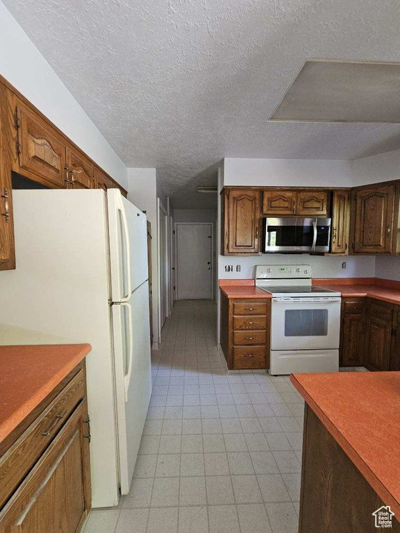 Kitchen featuring white appliances, a textured ceiling, light floors, and brown cabinetry