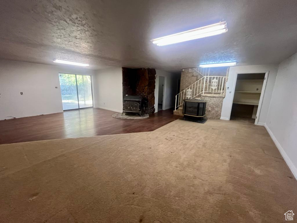 Living area featuring a wood stove, stairway, a textured ceiling, and carpet