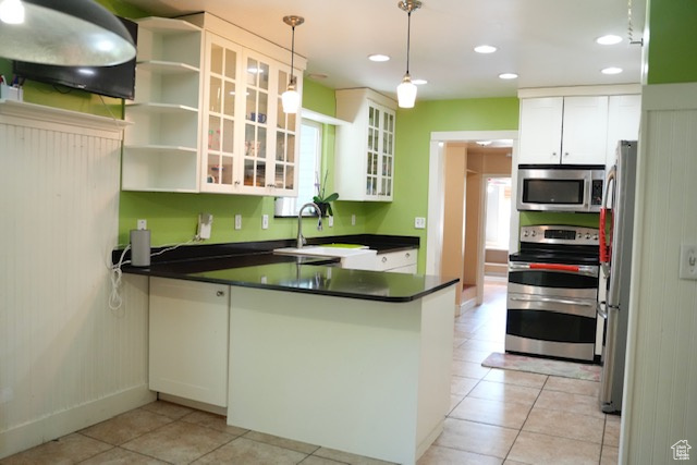 Kitchen with appliances with stainless steel finishes, a peninsula, a sink, dark countertops, and light tile patterned flooring