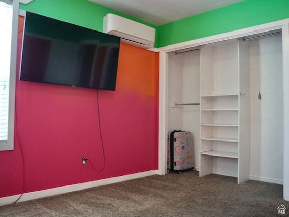 Unfurnished bedroom featuring an AC wall unit, carpet floors, a closet, and baseboards
