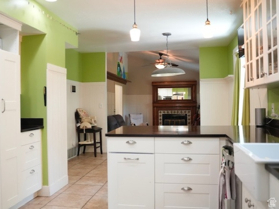 Kitchen featuring freestanding refrigerator, a wainscoted wall, ceiling fan, a fireplace, and dark countertops