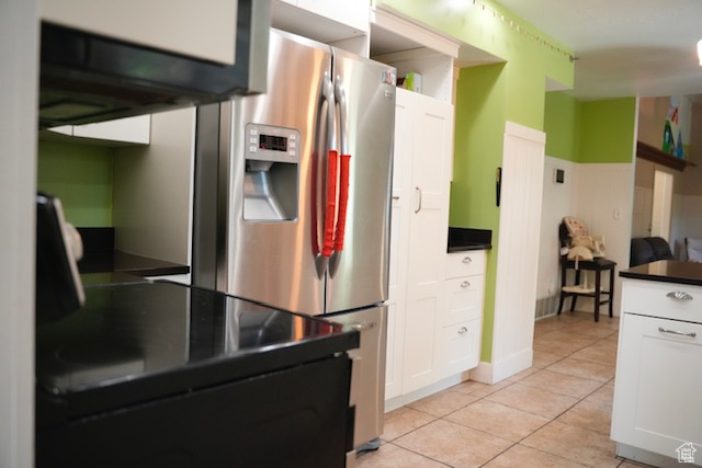 Kitchen with stainless steel fridge, dark countertops, light tile patterned floors, and white cabinets