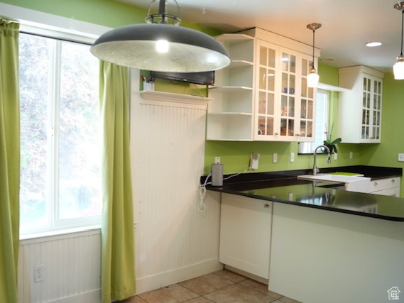 Kitchen with dark countertops, glass insert cabinets, white cabinets, light tile patterned flooring, and open shelves