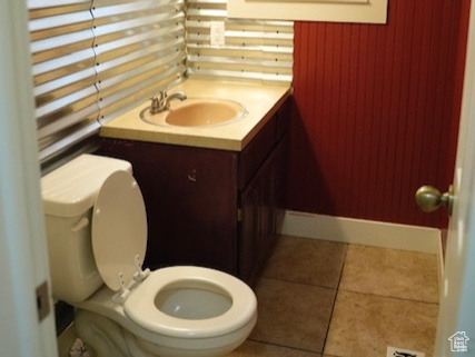 Half bathroom with toilet, wainscoting, vanity, and tile patterned flooring