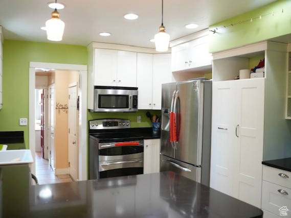 Kitchen with appliances with stainless steel finishes, white cabinetry, a sink, dark countertops, and recessed lighting