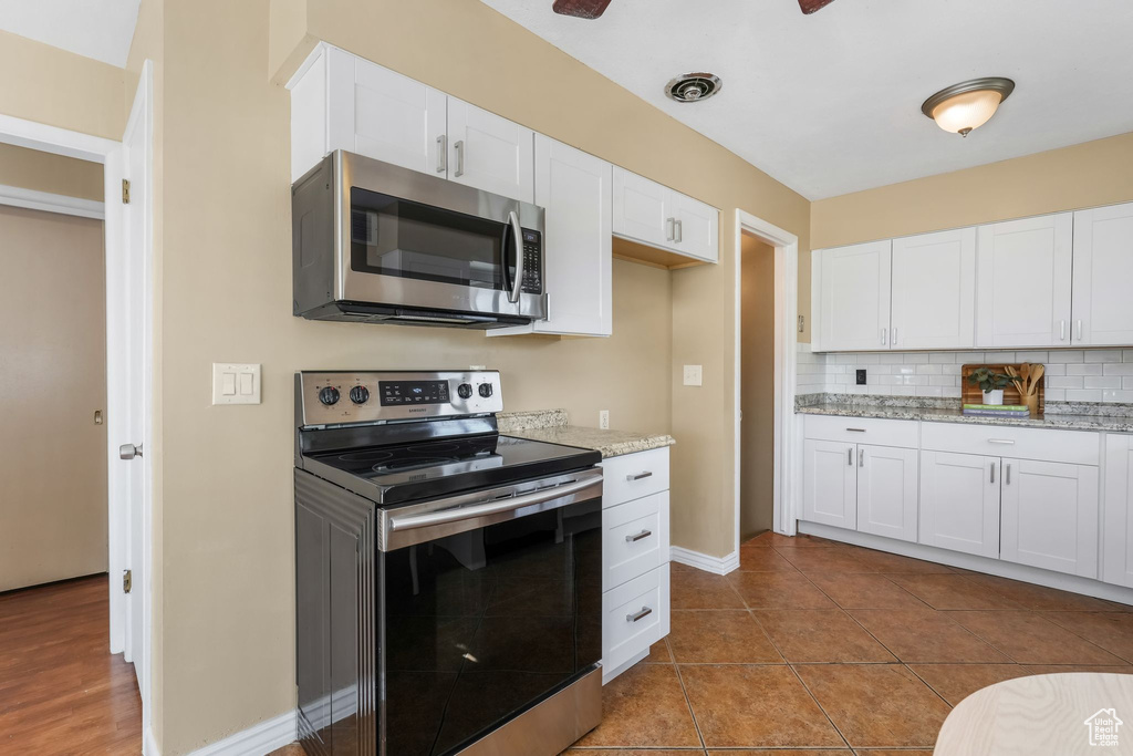 Kitchen with stainless steel appliances, white cabinets, backsplash, light stone counters, and baseboards