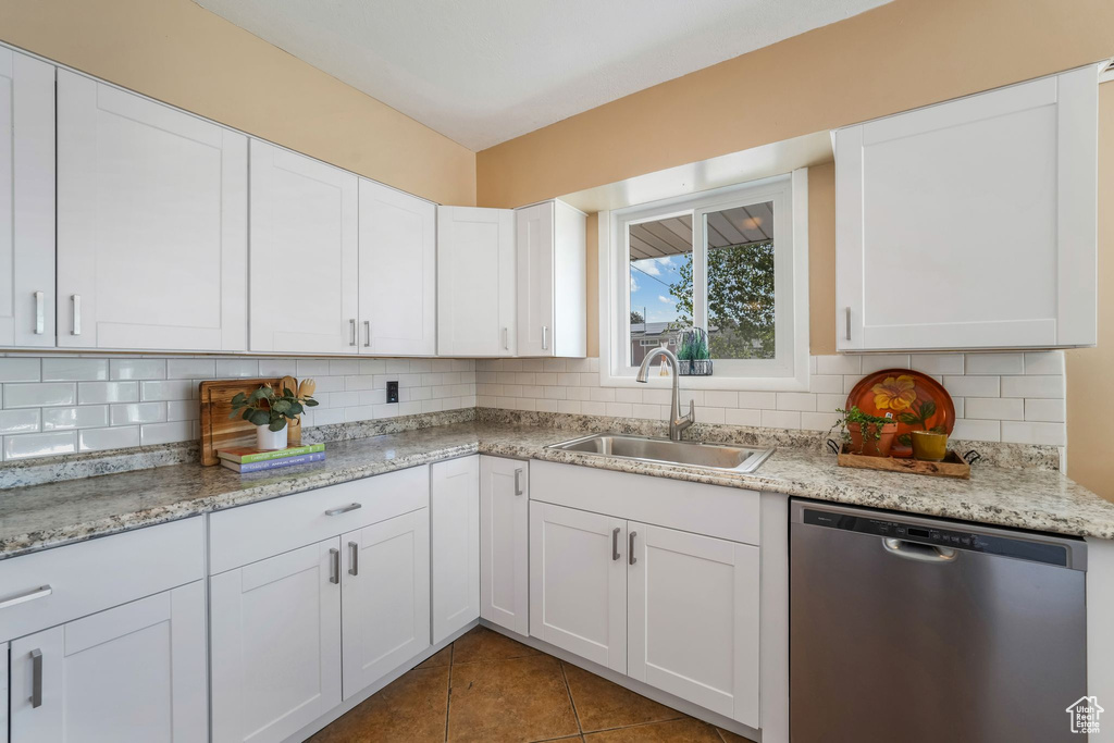 Kitchen featuring stainless steel dishwasher, a sink, tasteful backsplash, and white cabinetry