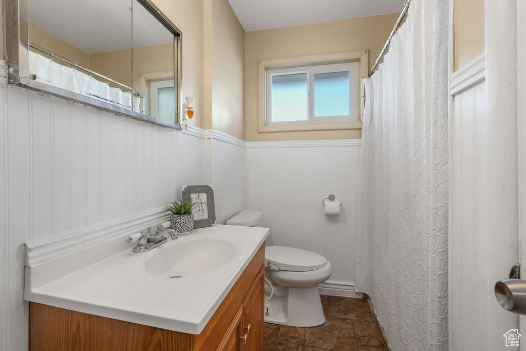 Bathroom featuring toilet, vanity, wainscoting, and stone finish floors