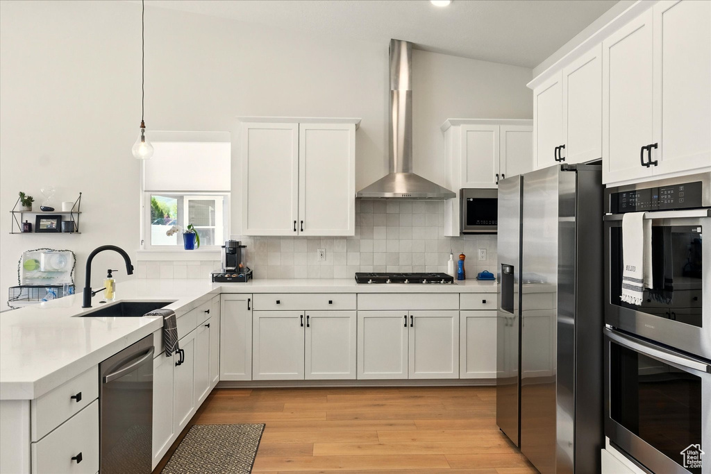 Kitchen with appliances with stainless steel finishes, wall chimney exhaust hood, a sink, a peninsula, and backsplash