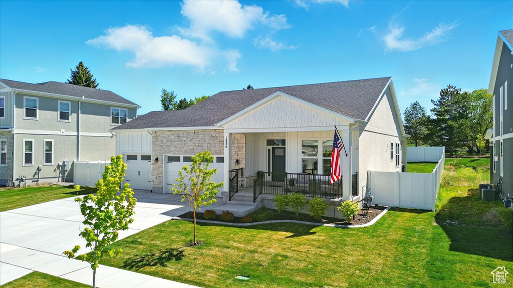 View of front facade with covered porch, concrete driveway, an attached garage, central AC, and stone siding