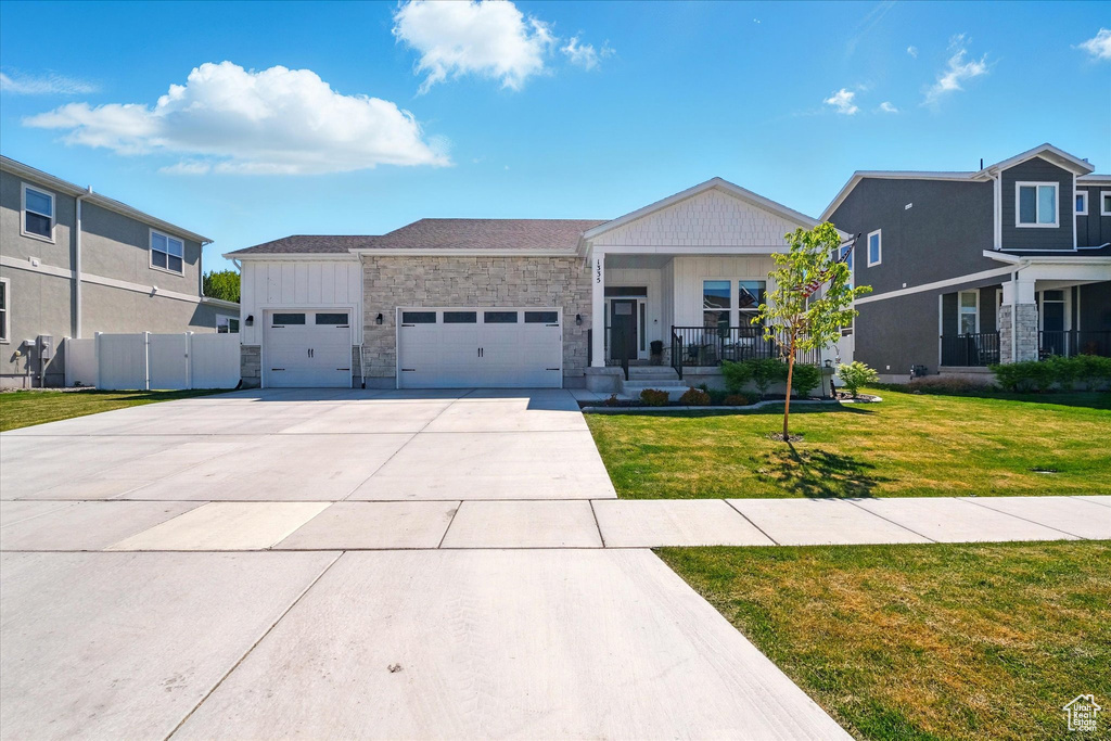 View of front of home with an attached garage, driveway, stone siding, covered porch, and board and batten siding