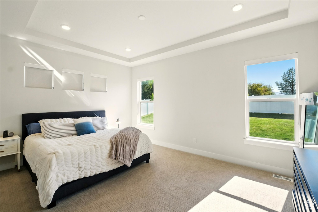 Bedroom with a tray ceiling, carpet floors, multiple windows, and recessed lighting