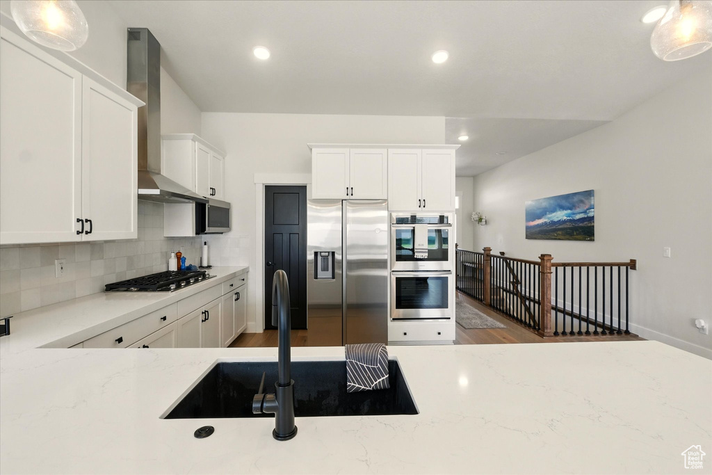 Kitchen featuring appliances with stainless steel finishes, wall chimney exhaust hood, backsplash, wood finished floors, and white cabinets