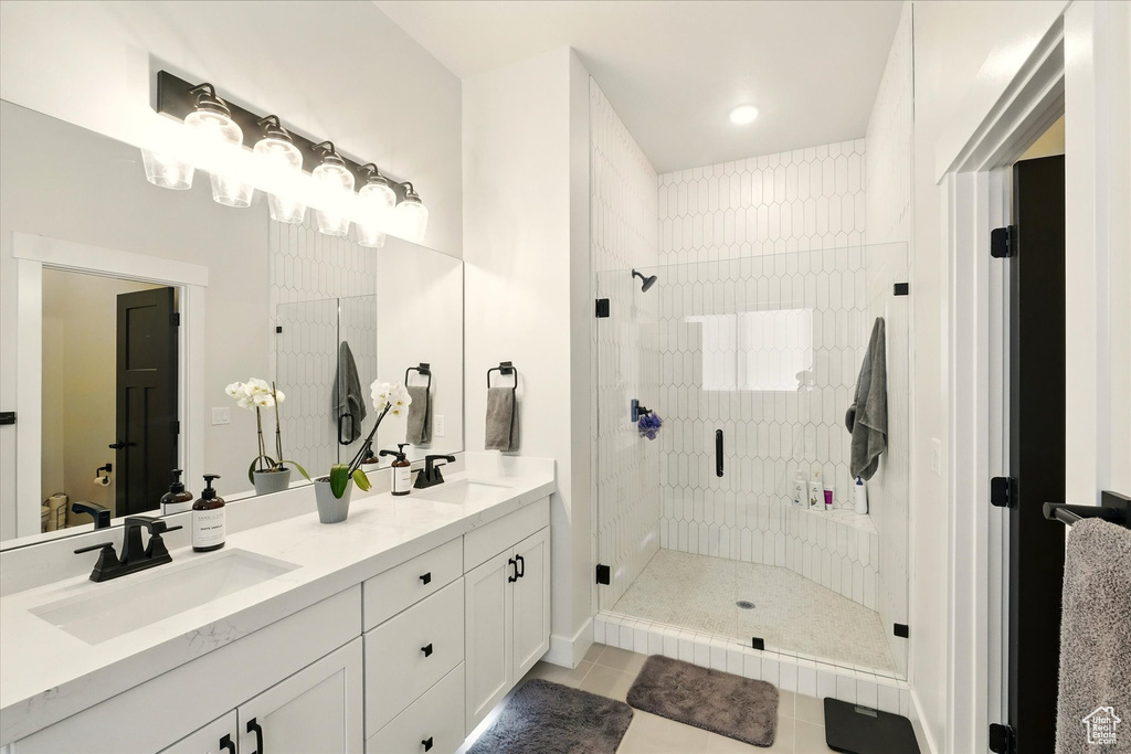 Bathroom with a shower stall, double vanity, tile patterned floors, and baseboards