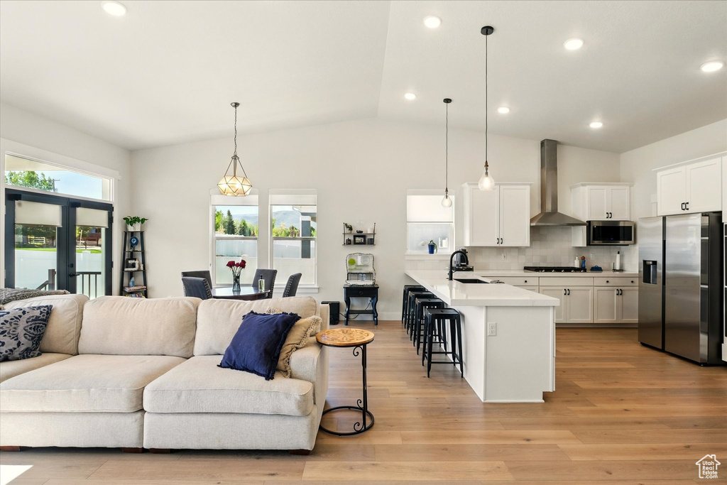 Kitchen featuring stainless steel appliances, wall chimney range hood, open floor plan, a kitchen bar, and a sink