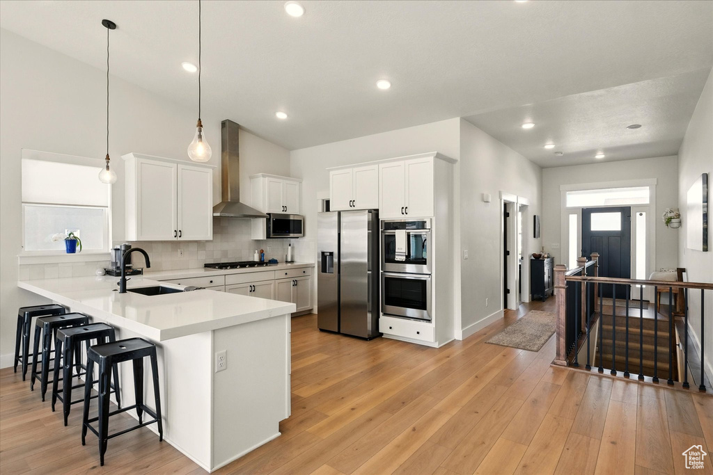 Kitchen featuring stainless steel appliances, wall chimney exhaust hood, a sink, a kitchen breakfast bar, and backsplash
