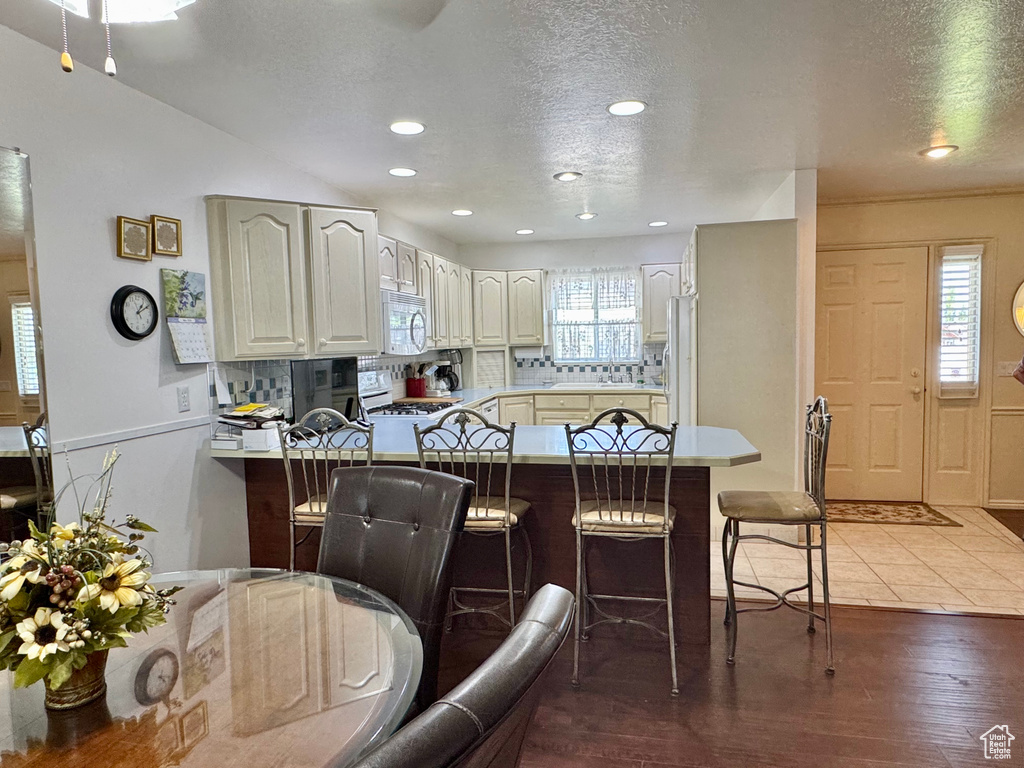 Kitchen featuring white appliances, a peninsula, a breakfast bar area, backsplash, and a textured ceiling