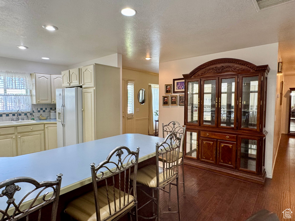 Kitchen with white refrigerator with ice dispenser, a kitchen bar, light countertops, decorative backsplash, and plenty of natural light
