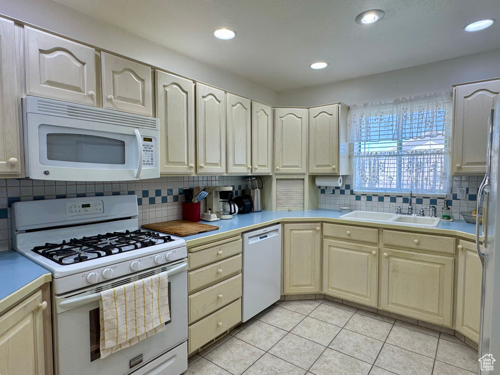 Kitchen featuring white appliances, decorative backsplash, light tile patterned flooring, a sink, and light countertops