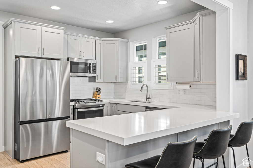 Kitchen with appliances with stainless steel finishes, a sink, a peninsula, light countertops, and recessed lighting
