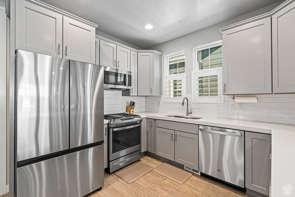 Kitchen featuring stainless steel appliances, a sink, light countertops, light wood-type flooring, and a textured ceiling