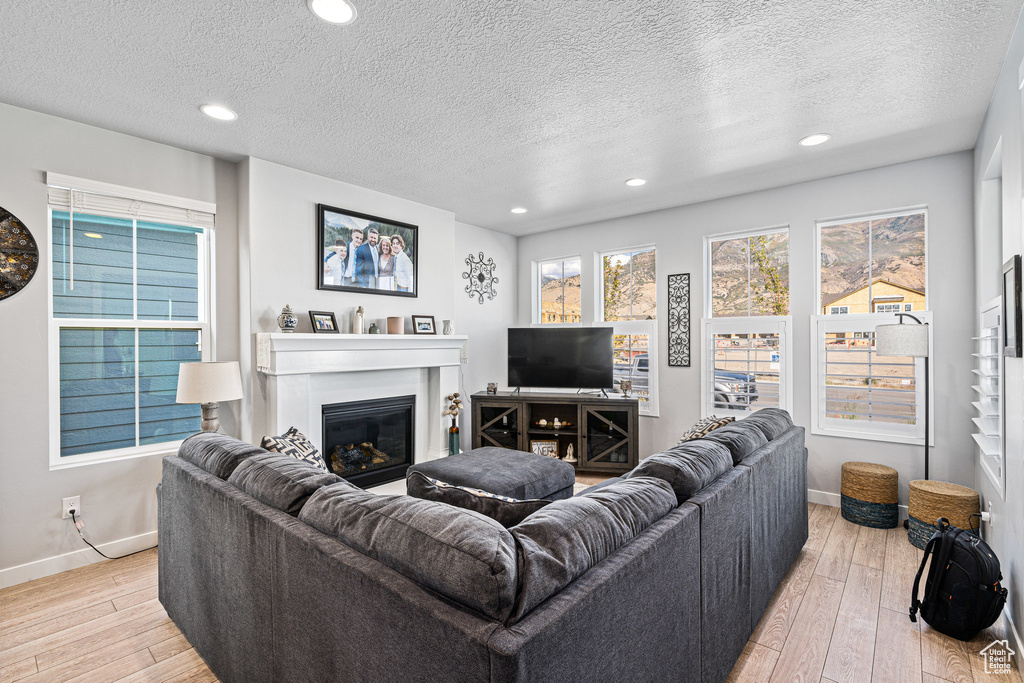 Living room featuring light wood-style floors, baseboards, a glass covered fireplace, a textured ceiling, and recessed lighting