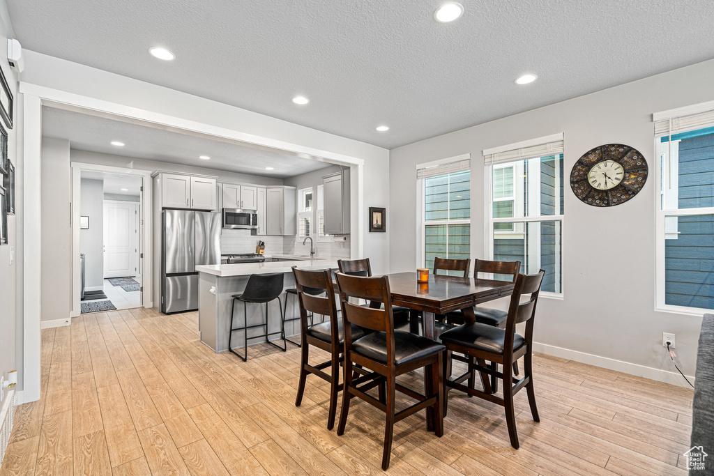 Dining area featuring light wood-style flooring, baseboards, recessed lighting, and a textured ceiling