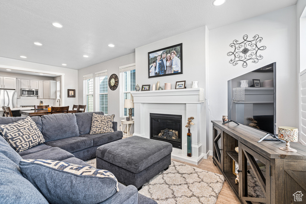Living area with light wood-style floors, recessed lighting, a glass covered fireplace, and a textured ceiling
