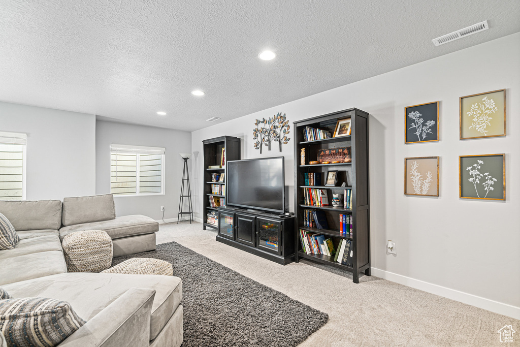Living room with a textured ceiling, baseboards, light colored carpet, and recessed lighting