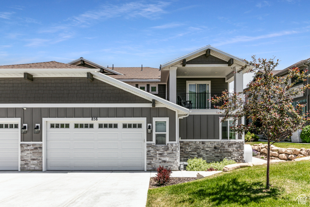 View of front of property featuring board and batten siding, stone siding, driveway, an attached garage, and a balcony