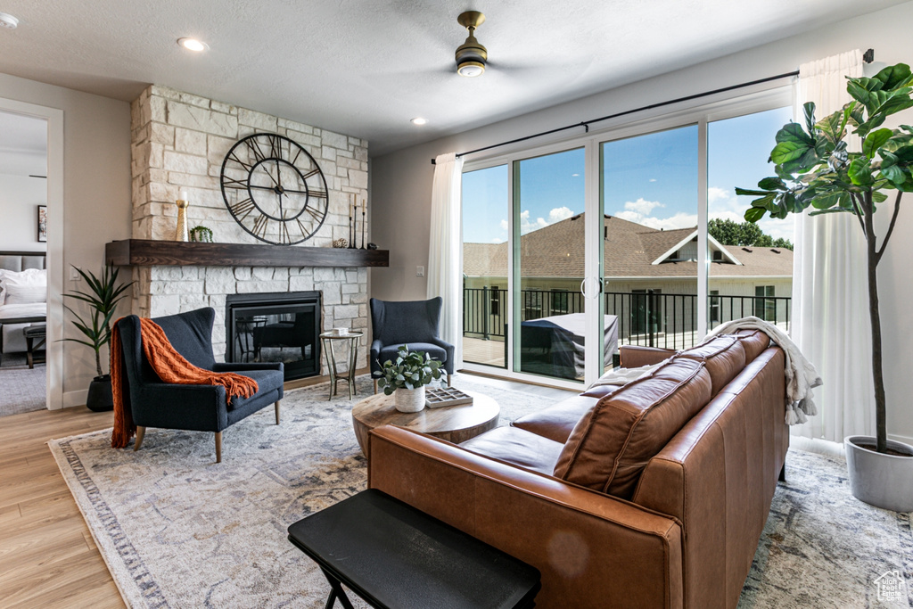 Living room featuring wood finished floors, ceiling fan, a stone fireplace, and recessed lighting
