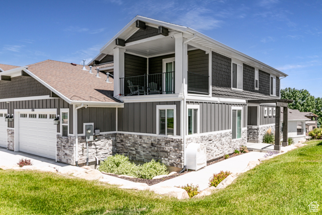 View of property exterior with a balcony, board and batten siding, a garage, stone siding, and a lawn