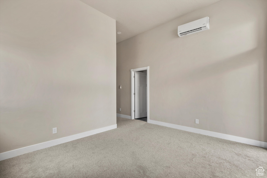 Empty room featuring a wall mounted air conditioner, carpet flooring, and baseboards