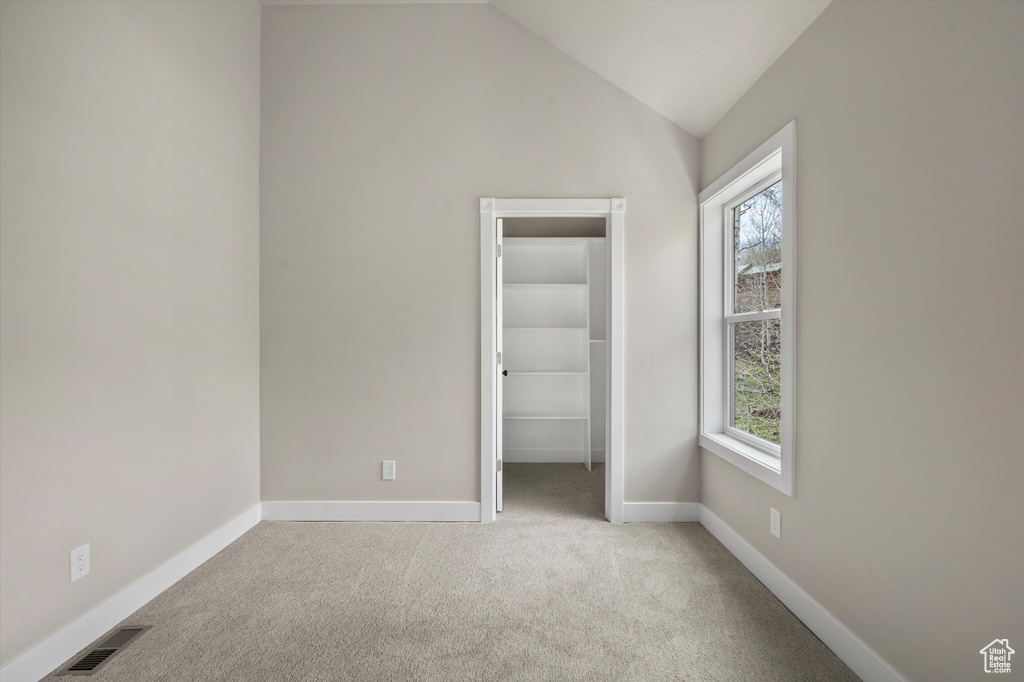 Unfurnished bedroom featuring a walk in closet, carpet floors, lofted ceiling, baseboards, and a closet