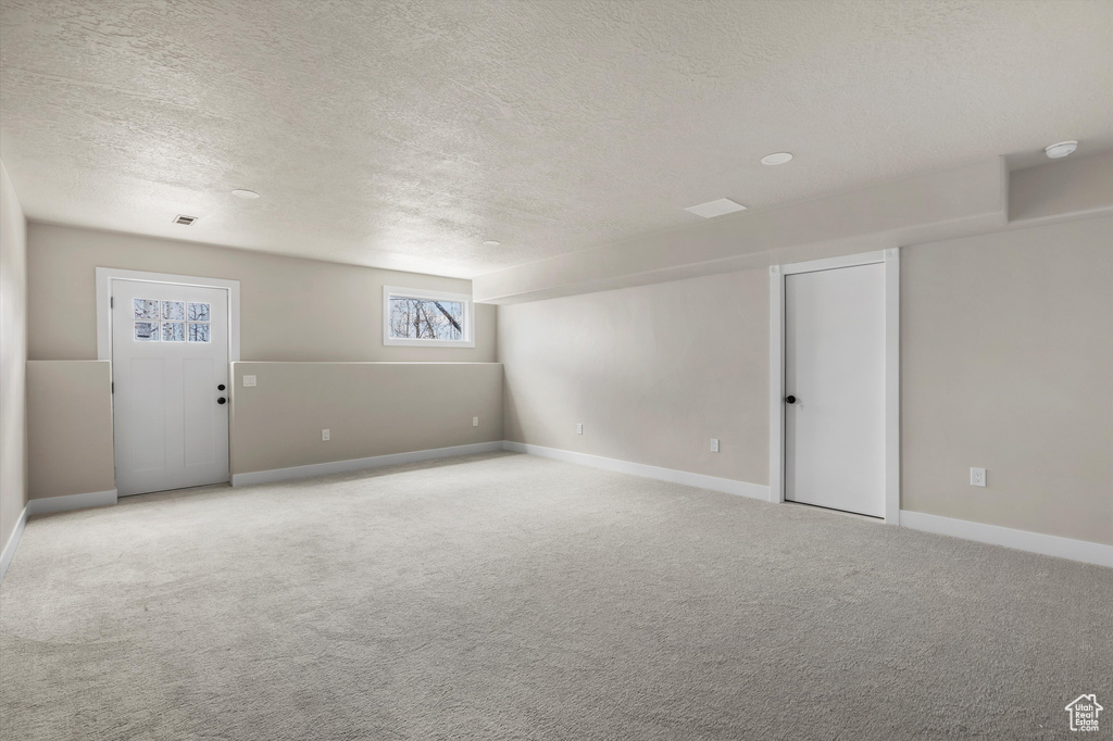 Carpeted spare room featuring a textured ceiling, baseboards, and a smoke detector