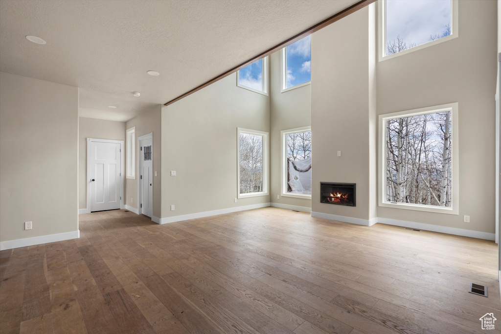 Unfurnished living room with hardwood / wood-style flooring, a glass covered fireplace, a towering ceiling, and baseboards