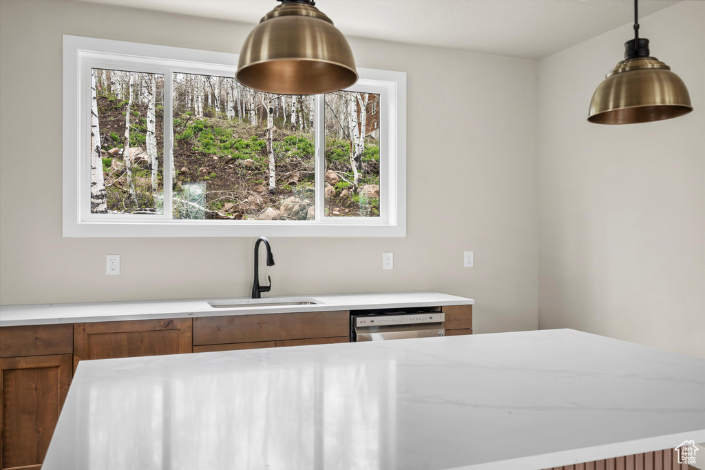 Kitchen with a sink, brown cabinets, dishwashing machine, and hanging light fixtures