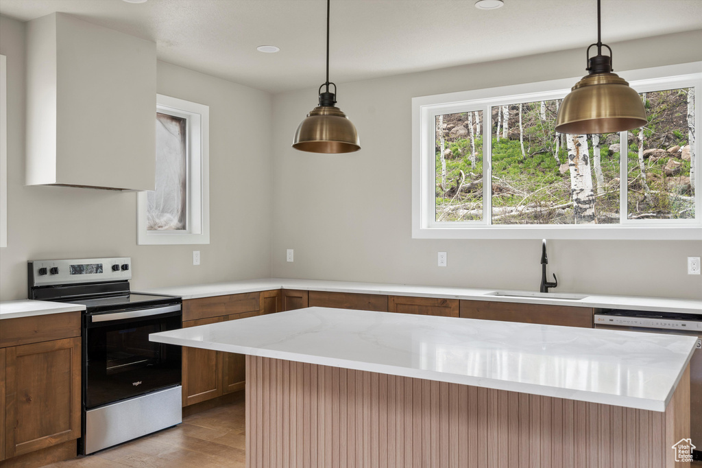 Kitchen with stainless steel range with electric cooktop, a sink, light wood-type flooring, dishwashing machine, and brown cabinetry