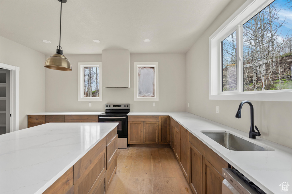 Kitchen with stainless steel appliances, a sink, brown cabinetry, light wood-type flooring, and light stone counters