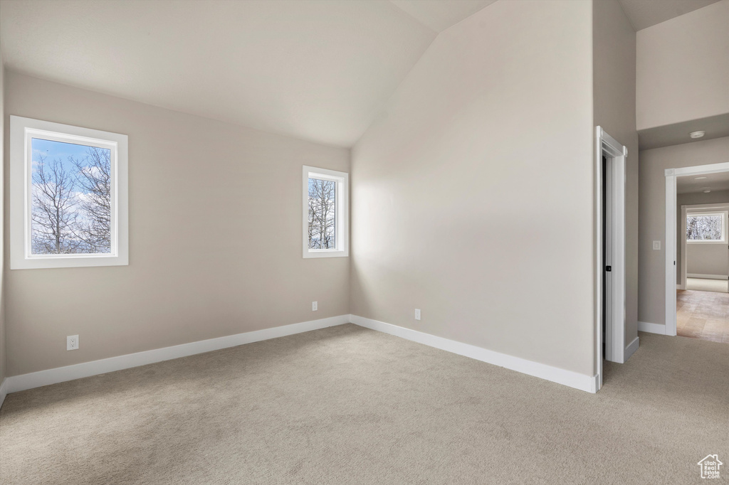 Unfurnished room featuring light colored carpet, baseboards, and high vaulted ceiling