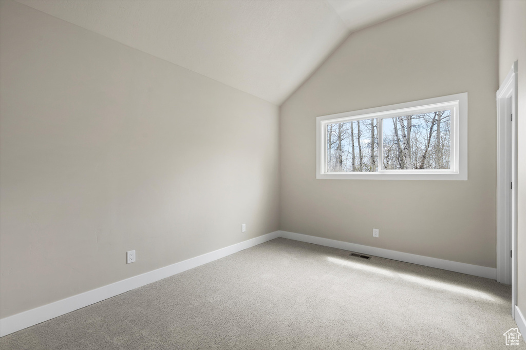 Carpeted spare room featuring lofted ceiling and baseboards