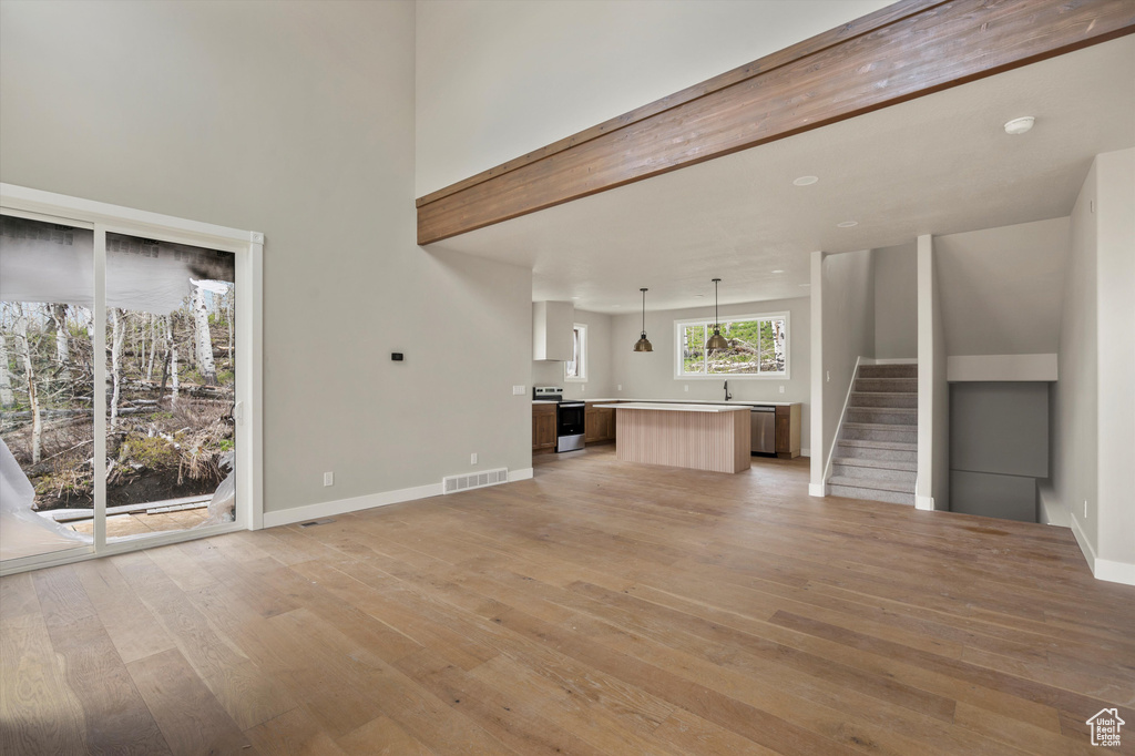 Unfurnished living room featuring light wood-style floors, baseboards, stairway, a sink, and a towering ceiling