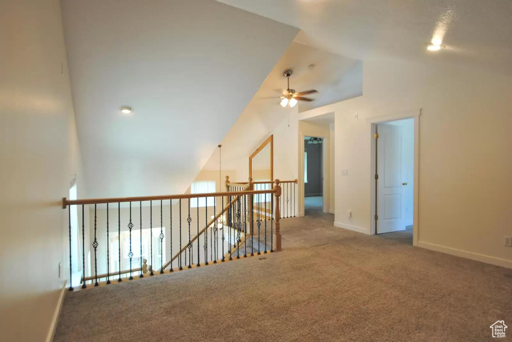 Carpeted empty room featuring ceiling fan, lofted ceiling, and baseboards