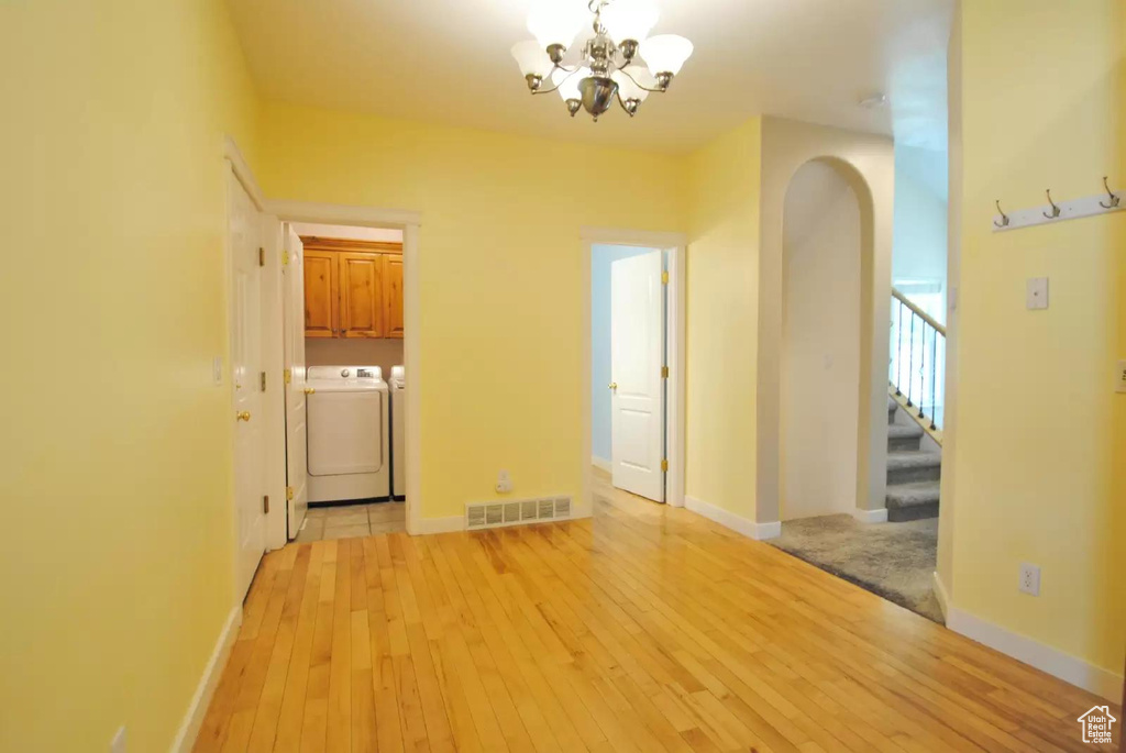 Empty room featuring independent washer and dryer, a chandelier, arched walkways, stairway, and light wood-style flooring