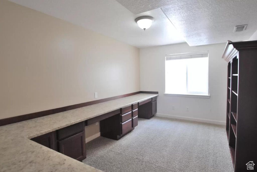 Unfurnished office featuring built in desk, a textured ceiling, light colored carpet, and baseboards