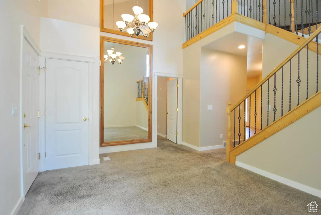 Carpeted foyer entrance featuring a chandelier, a high ceiling, stairs, and baseboards