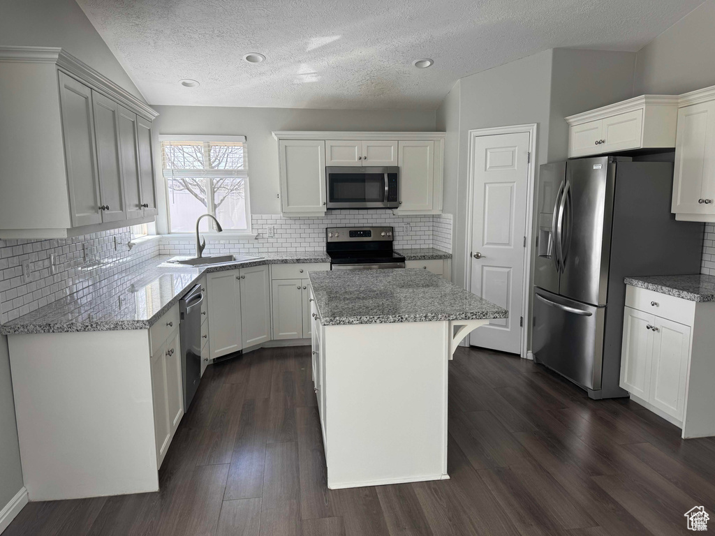 Kitchen featuring stainless steel appliances, a sink, a center island, light stone countertops, and a textured ceiling