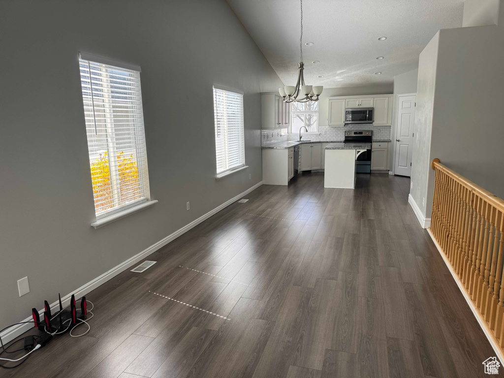 Unfurnished dining area with a chandelier, a sink, dark wood finished floors, vaulted ceiling, and baseboards
